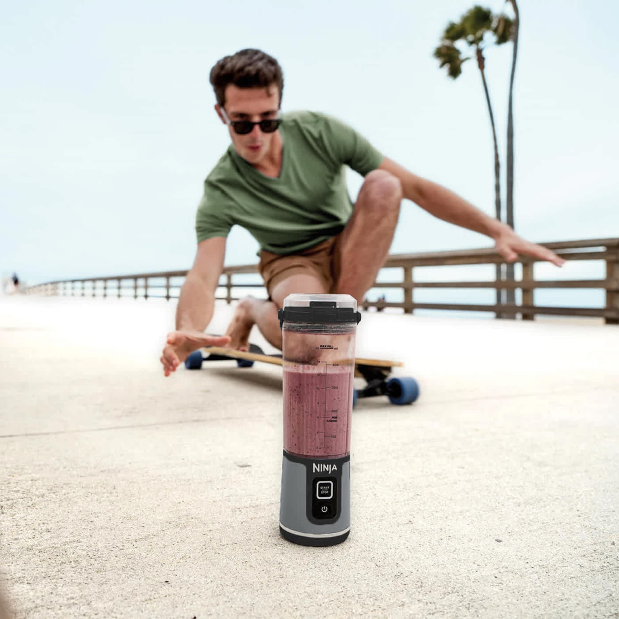 Blendern med smoothie på en strandpromenad