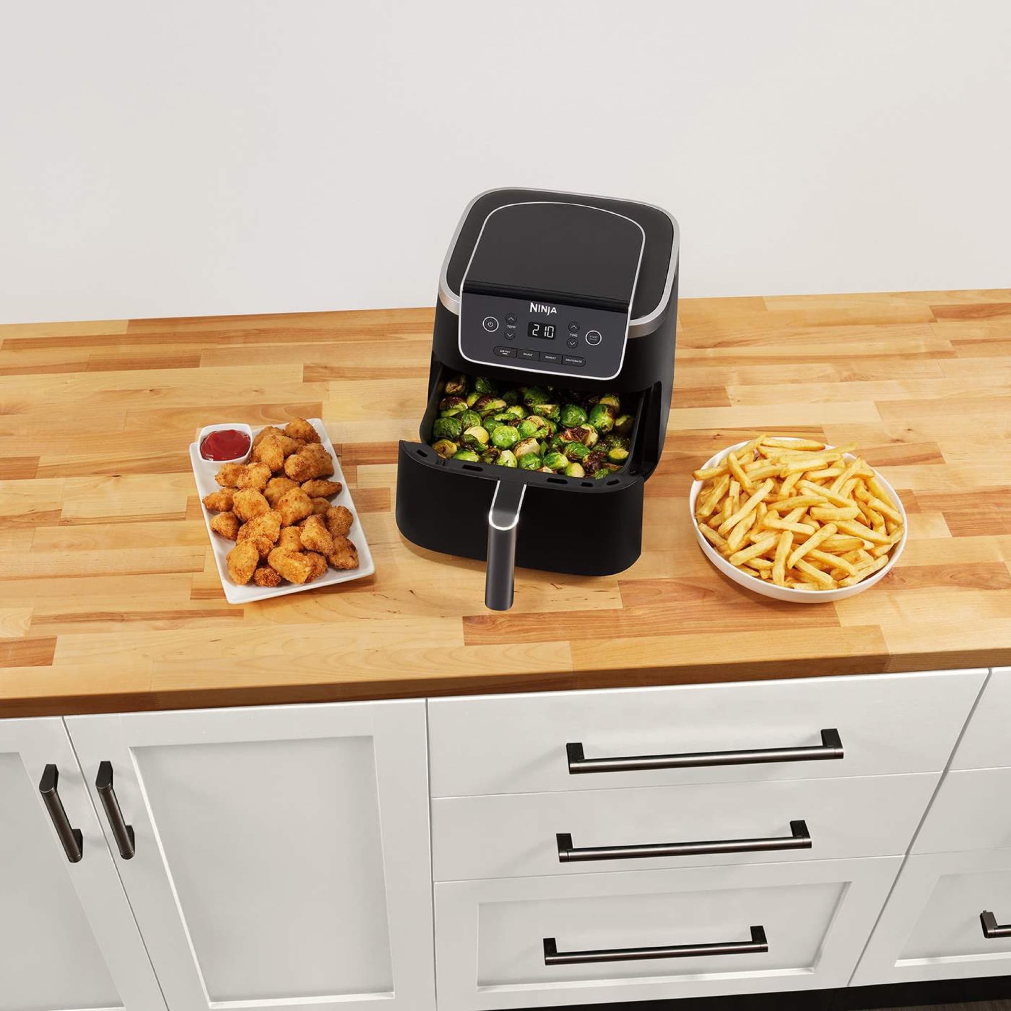 Airfryern på köksbänken med brysselkål i lådan, kyckling och pommes bredvid