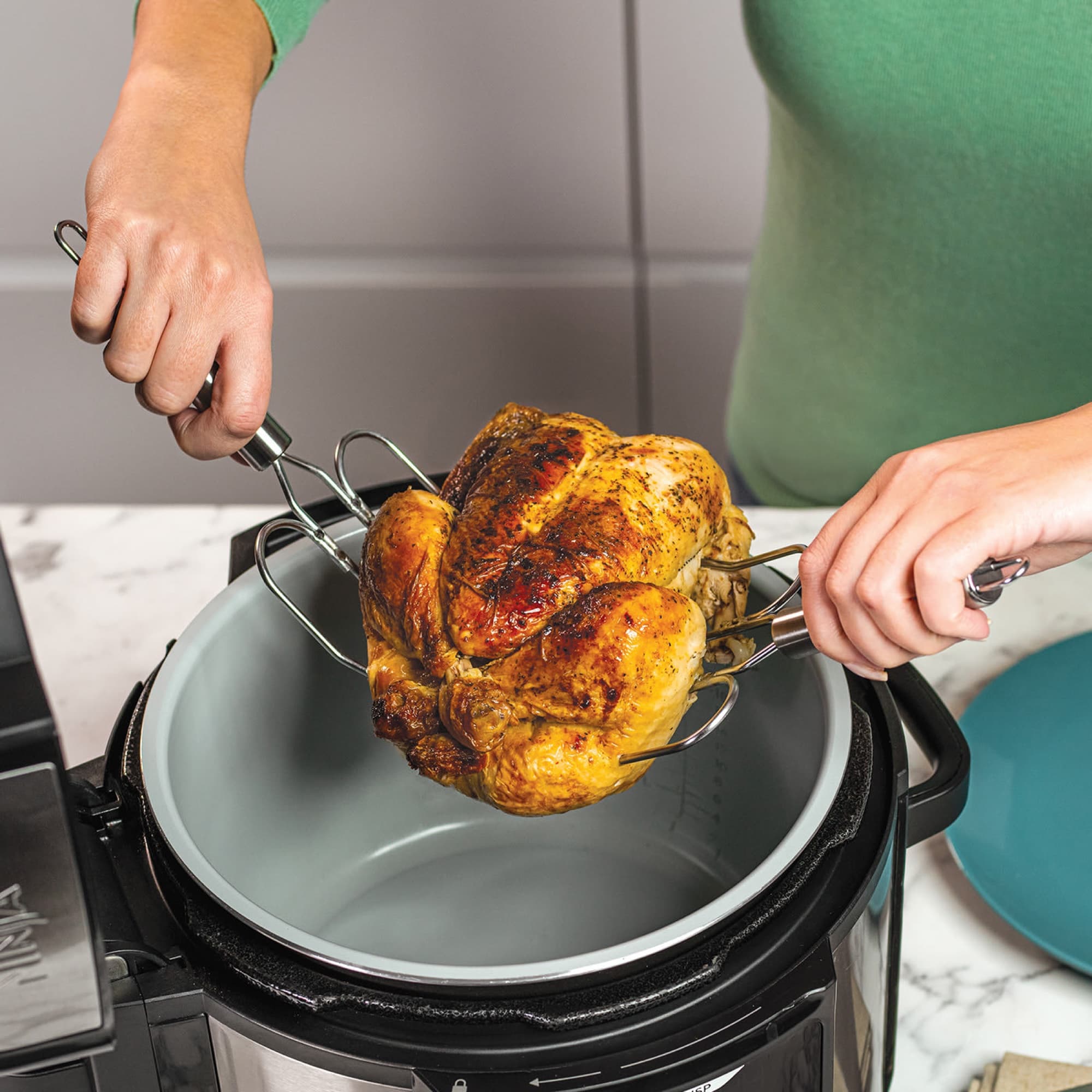 A roast chicken lifted out of the pot with the forks